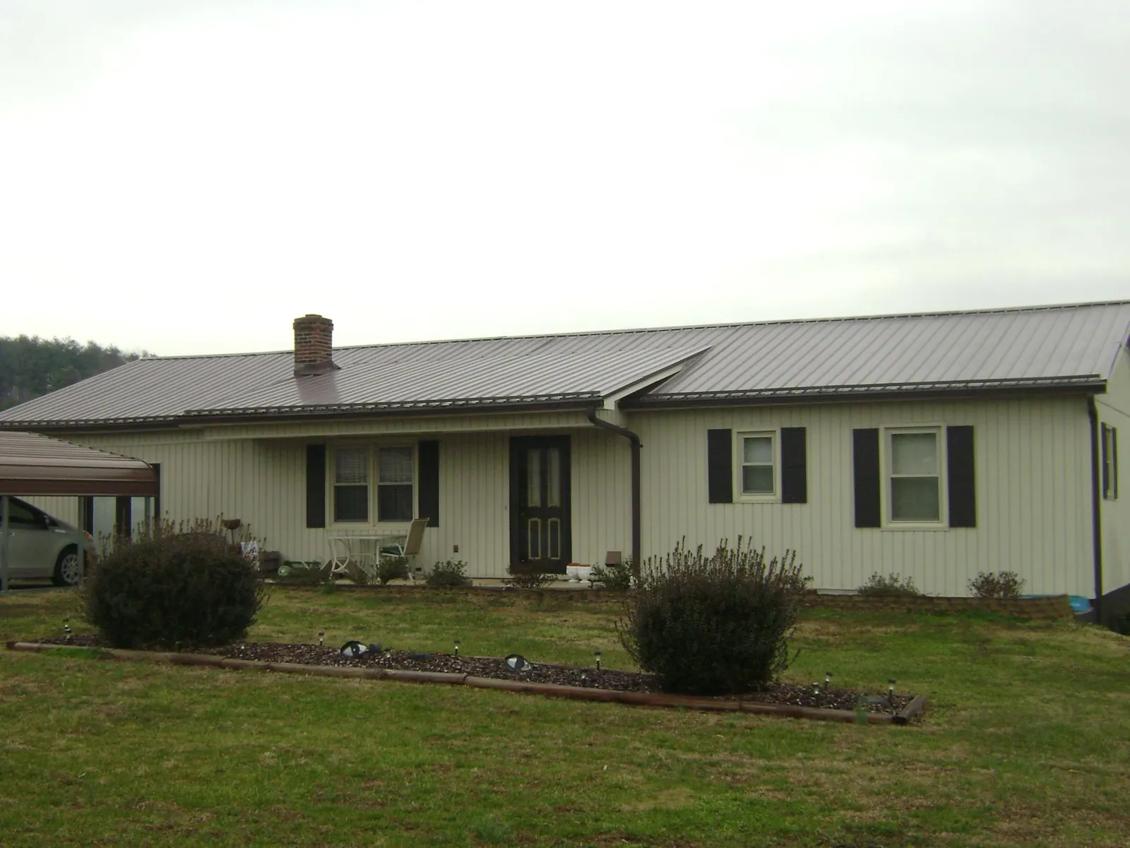 Brown metal roof on a cream sided ranch home with a brick chimney in Auburn